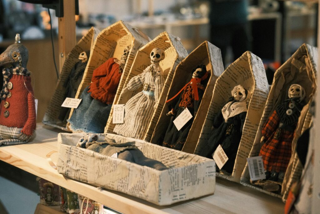 Unique handcrafted skeleton dolls displayed in decorative paper coffin boxes at a market stall.